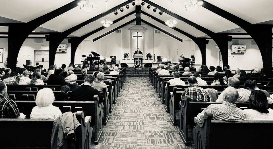 Congregation gathered for Sunday morning worship at Zion Baptist Church, with the pastor preaching beneath a wooden cross